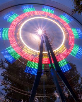 Rotating Ferris wheel in a night park with neon lighting against the sky.