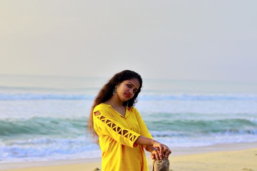 A stylish girl standing on the seashore holding a dry tree wood