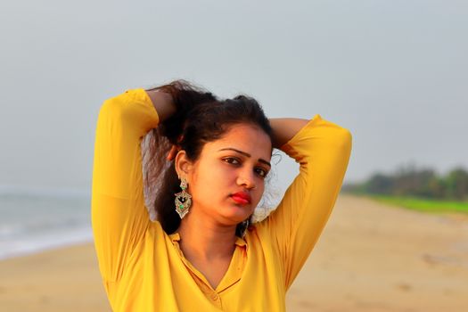 A asian beautiful girl standing on the beach and holding her hairs with yellow top, head shot