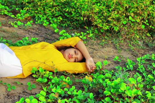 A fashionable young girl lying on the ground among green leaves