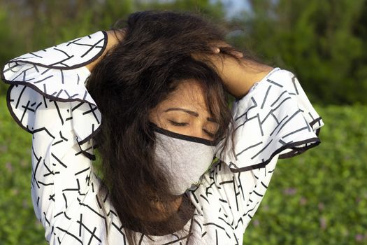 stylish Woman wearing protective face mask and posing on outdoors natural green background.