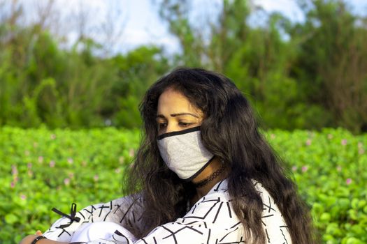 Portrait of a stylish young girl sitting in the nature and wearing face mask Protection against disease, coronavirus.