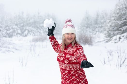 Woman wearing red snowflake sweater and beanie is throwing a huge snowball