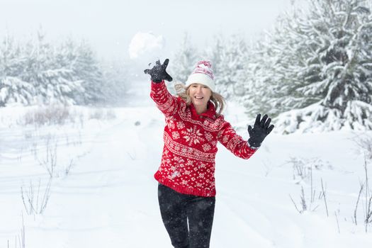 Happy woman wearing a red and white snowflake sweater and beanie playfully throwing a snowball