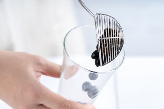 Making bubble tea, scoop and pour cooked brown sugar flavor tapioca pearl bubble balls into cup on white wooden table background, close up, copy space.