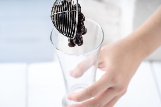 Making bubble tea, scoop and pour cooked brown sugar flavor tapioca pearl bubble balls into cup on white wooden table background, close up, copy space.