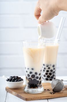 Making bubble tea, scoop and pour cooked brown sugar flavor tapioca pearl bubble balls into cup on white wooden table background, close up, copy space.