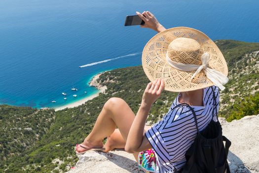 Active sporty woman on summer vacations taking selfie picture while enjoying beautiful coastal view of Cres island, Croatia from Lubenice traditional costal village.