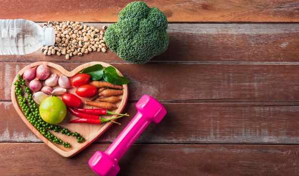 Top view of various fresh organic fruit and vegetable in heart plate and sports shoes, dumbbell and water, studio shot on wooden gym table, Healthy diet vegetarian food concept, World food day