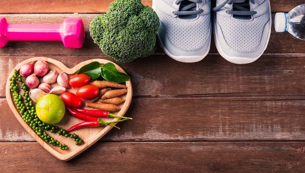 Top view of various fresh organic fruit and vegetable in heart plate and sports shoes, dumbbell and water, studio shot on wooden gym table, Healthy diet vegetarian food concept, World food day