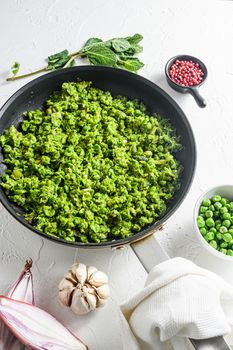 Mushy peas recipe cooked frying pan and peas in bowl with mint shallot pepper and salt over white stone surface organic keto food photo side view close up.