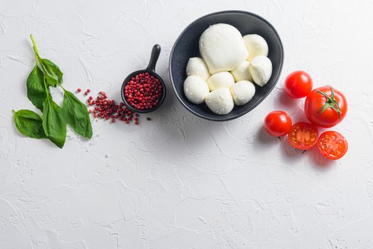 Raw ripe Mozzarella cheese balls with fresh basil leaves and cherry tomatoes, the ingredients , on white background top view space for text.