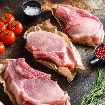 Tree bunch raw pork chops arranged with herbs, oil and spices. Cooking meat. On dark background Square