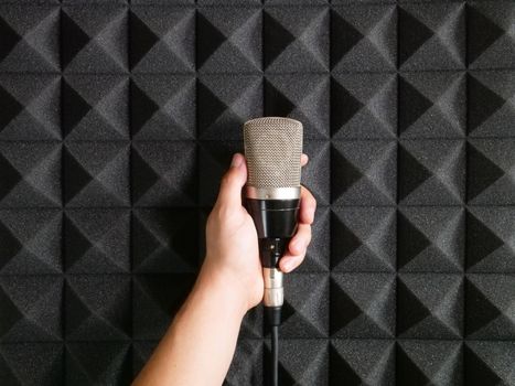 Hand holding microphone against professional acoustic foam