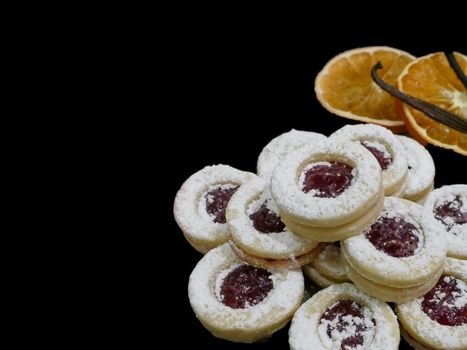 Strawberry Christmas biscuits and orange slices with cinnamon sticks on a black background.