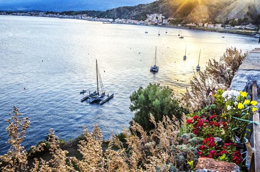 Boats sailing at sunset along the cliffs coast near the city of taormina sicily italy