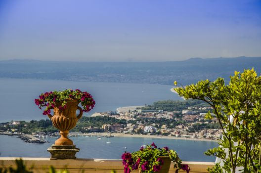 Flowers in pot with a background of the sicilian coast at the height of the city of taormina italy