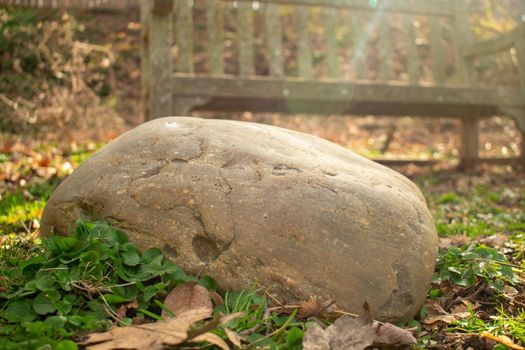 A Smooth Grey Rock in Front of an Old Wooden Park Bench