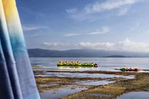 Pedal boats , canoes and life boat on the shore of Lake Trasimeno -Italy- ,in the foreground part of beach umbrella