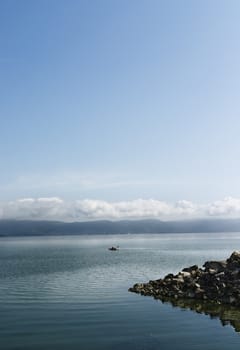 Trasimeno Lake with a sailing canoe , in the foreground seawall in the background lake coast