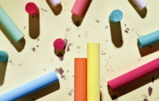 Multicolored thick sticks of chalk on colored background , in the foreground two pieces orange and yellow in focus