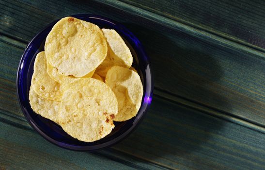 Potato chips or crisps ina blue bowl on dark wooden table,beautiful slices of fried potatoes