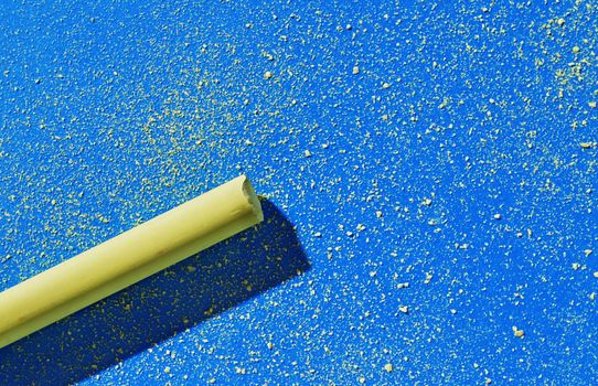 Yellow thick stick of chalk on blue background , small pieces of yellow chalk scattered on the background
