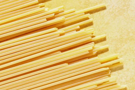 Bunch of dried spaghetti on yellow background , long thin cylindrical noodle pasta