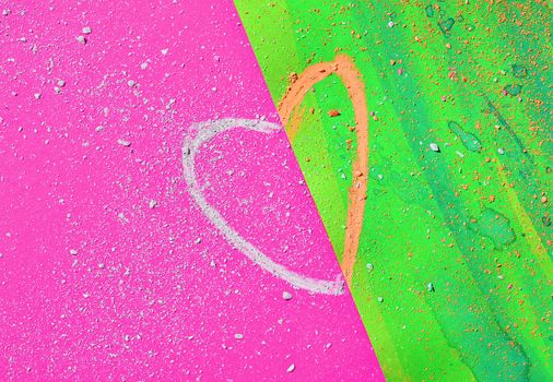 Drawing a heart with orange and white chalk on pink and green paper ,small pieces of chalk scattered on paper