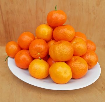 A plate full of clementines, on a wooden background