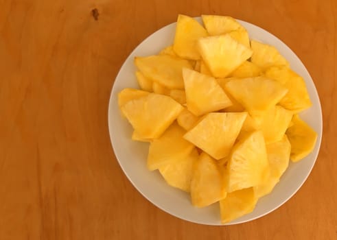 Pineapple sliced in a plate, on a wooden background.