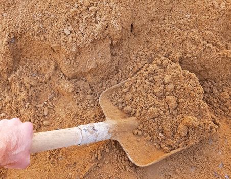 The shovel full of sand in the hand of the worker.