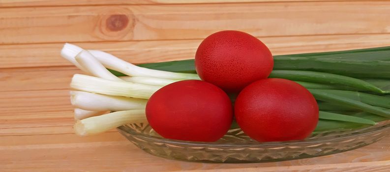 Spring onions and Easter red eggs on wooden background.