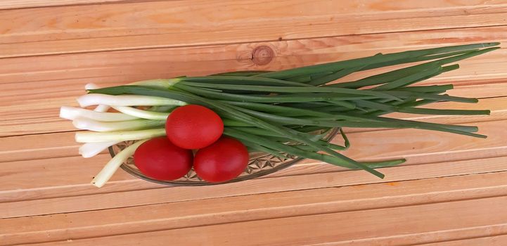 Spring onions and Easter red eggs on wooden background.