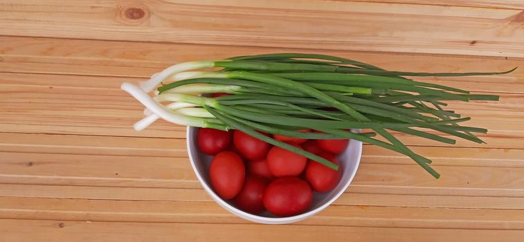 Spring onions and Easter red eggs on wooden background.