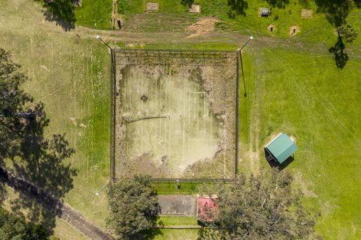 An aerial view of an old unused tennis court in disrepair in a public park in a small regional township