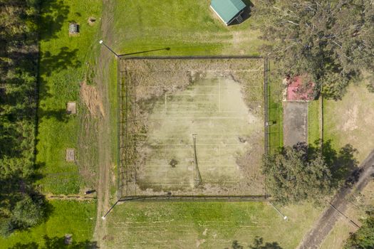 An aerial view of an old unused tennis court in disrepair in a public park in a small regional township