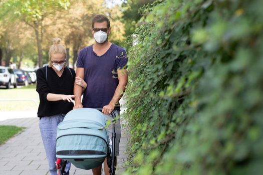 Worried young parent walking on empty street with stroller wearing medical masks to protect them from corona virus. Social distancing life during corona virus pandemic.