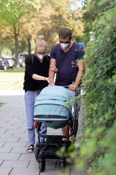Worried young parent walking on empty street with stroller wearing medical masks to protect them from corona virus. Social distancing life during corona virus pandemic.