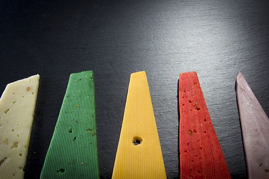 Pieces of colorful cheeses on black wooden background