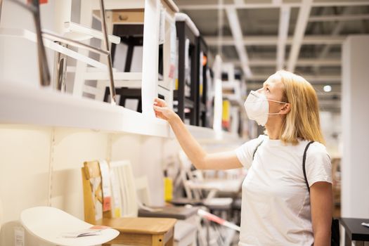 New normal during covid epidemic. Caucasian woman shopping at retail furniture and home accessories store wearing protective medical face mask to prevent spreading of corona virus.