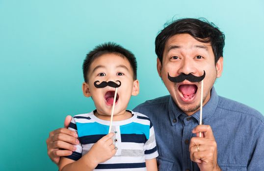 Family funny happy hipster father and his son kid holding black mustache props for the photo booth close face, studio shot isolated on a blue background, November men health awareness