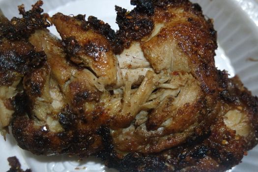 Close up of roasted chicken pieces in a white plate served for meal. Meat background for restaurant advertisements