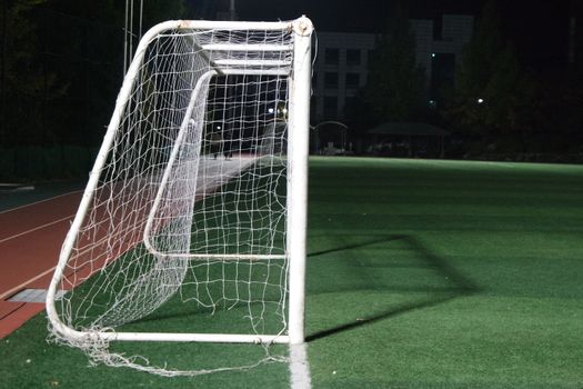 Night view of a soccer goal net under flood lights. Closeup view of goal net in a soccer playground