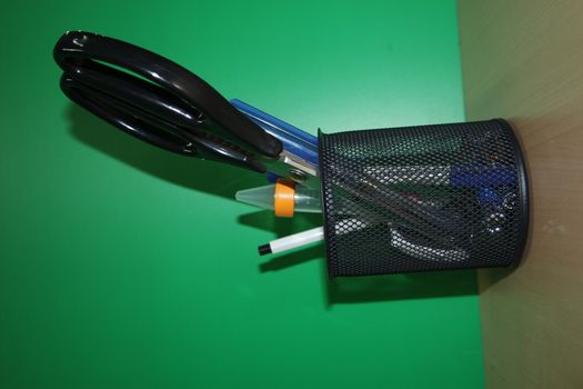 Closeup view of a stationery pot containing stationery items. stationery pot in front of a green background.