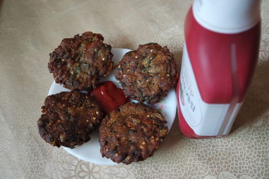 Delicious spicy fried round kebab served in white ceramic plate on a wooden floor with red sauce.
