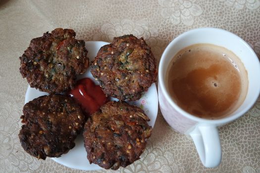 Delicious spicy fried round kebab served in white ceramic plate on a wooden floor with cup of hot tea.