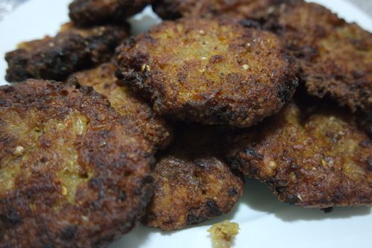 Delicious spicy fried round kebab served in a white ceramic plate on wooden floor