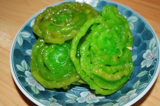 Crispy sweet Asian dessert green Jalebi cooked and served in ceramic plate, Indian sweet street food with juicy syrup, a closeup view.
