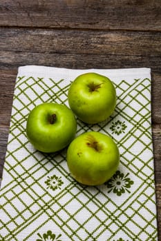 Ripe green apples on a rustic napkin on wooden table.